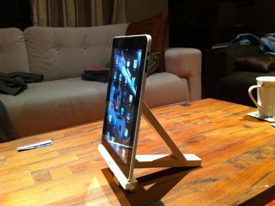 An iPad set on top of a hackers IKEA easel on a wooden table with a tan couch in the background