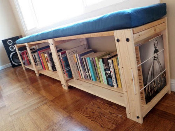 An IKEA hacked shelf for books running the length of a window with a blue cushion on top and a speaker in the corner, all shot at an angle