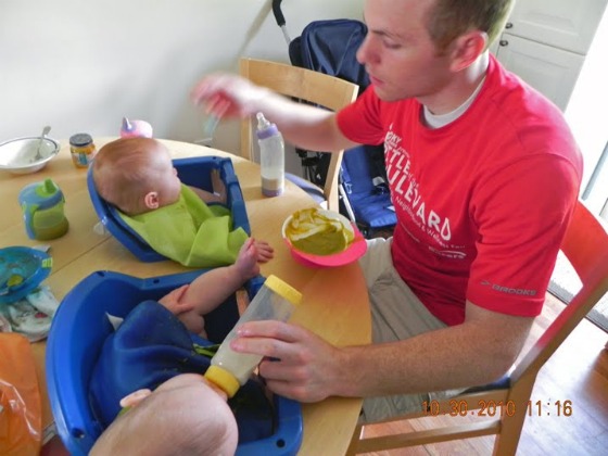 A dad with his two twin boys feeds them simultaneously a an IKEA hack table affixed with two high chair set into it