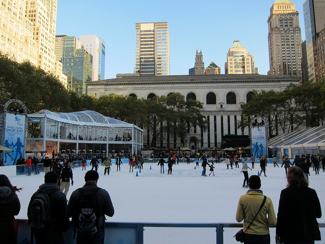 Under clear blue skies, New York ice skaters enjoy the ice skating rink at Bryant Park in Midtown NYC