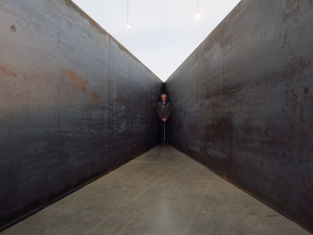 Man standing in a corner of Richard Serra Gagosian exhibition where 7 plates of gigantic steel walls meet at 6 angles