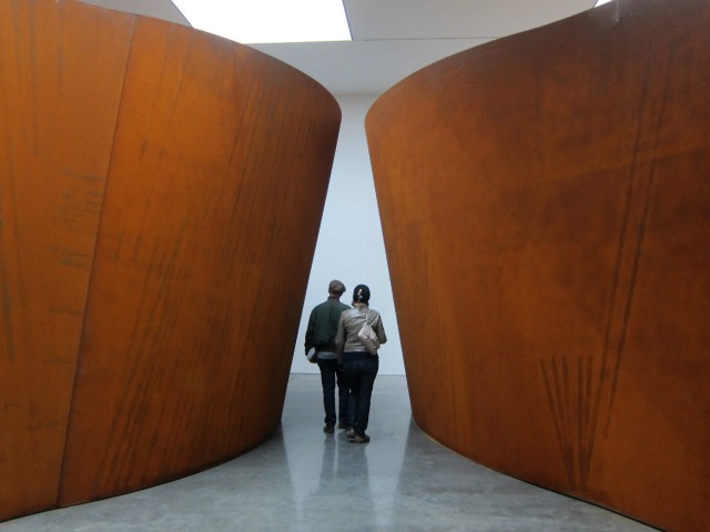 A man and a women walking through the hallway between serra's large steel scultpures at Gagosian gallery