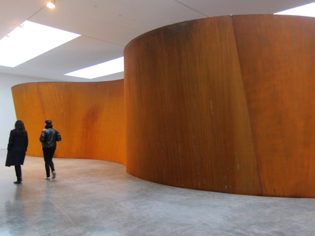 Richard Serra's Inside Out Sculpture, with talls orange steel walls towering over two people walking passed