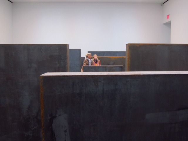 Two women walking together through Serra's large steel blocks.