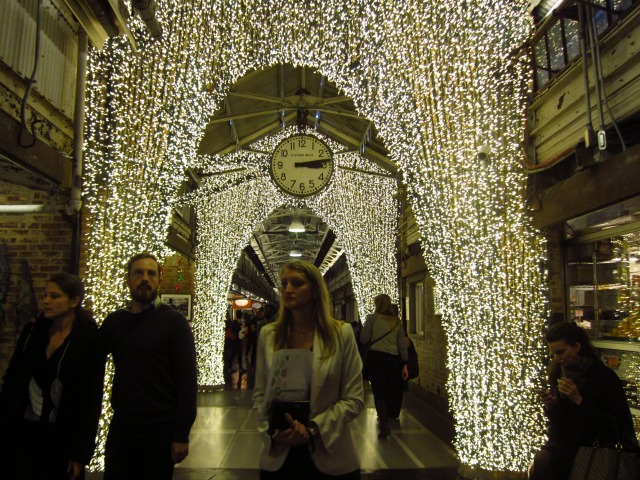 People walking through the Christmas lights lit hallways of Chelsea Market, getting their last minute shopping done