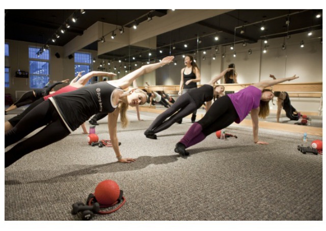 A class at Pure Barre hold a full side plank with their arm stretch out above their heads