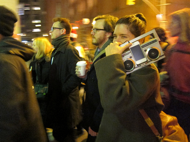 Women smiling and carrying a boombox on her shoulder playing the Kline composition for Unsilent Night