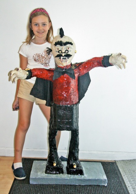 At NYC's Art Center, a young girl stands next to her completed art project of a vampire statue