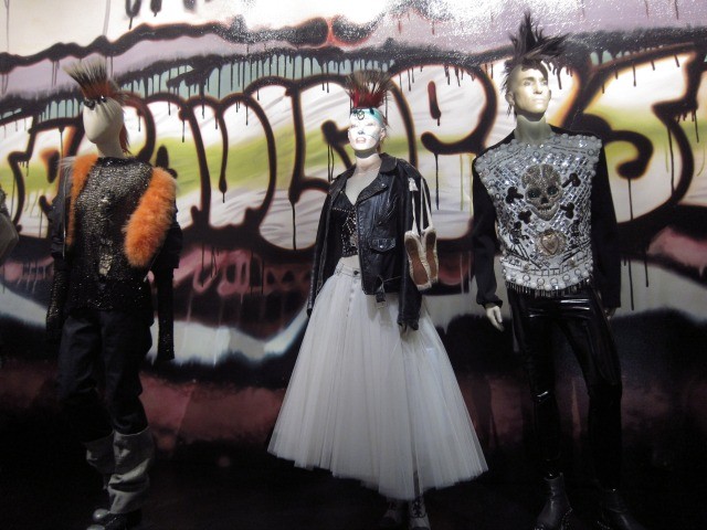 Image of the Jean Paul Gaultier exhibition's mannequins dressed up in punk fashion standing in front of graffiti