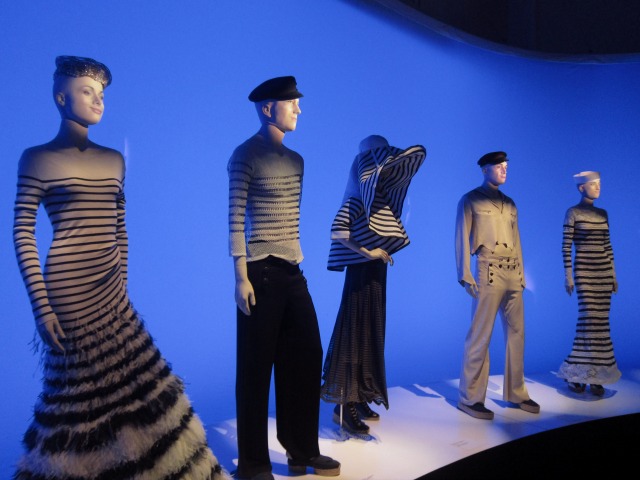 Image of the Jean Paul Gaultier exhibition's mannequins dressed up like sailors standing in front of a blue screen