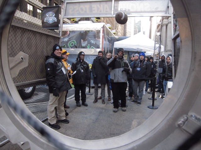 New Yorkers gather around one of the Super Bowl Boulevard games to toss a football through the tire.