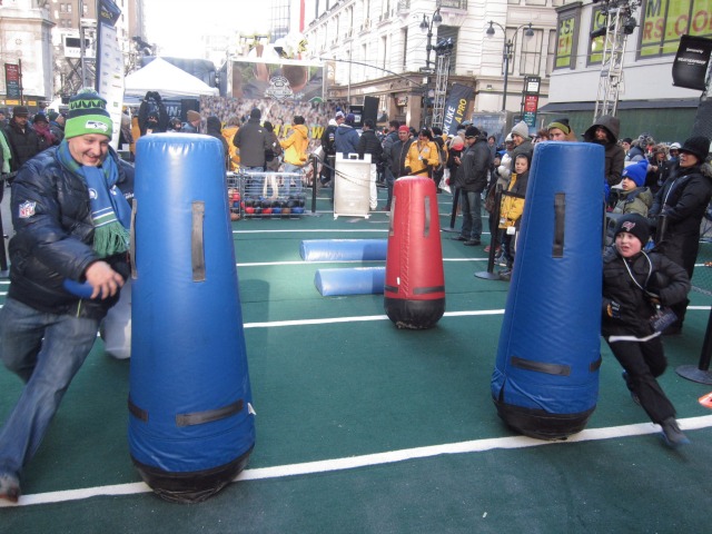 Football fans run through an obstacle course of punching bags in Times Square's Super Bowl Boulevard