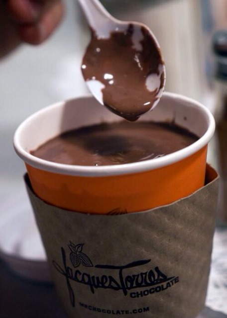 A spoon covered in chocolate and dripping into a to-go cup of hot chocolate from Jacques Torres