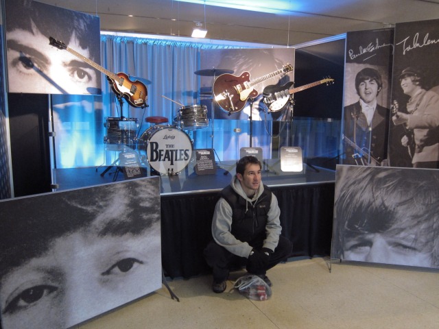 Image of a guy posing in front of the actual instruments used by The Beatles from the Fab Four's first Ed Sullivan appearance