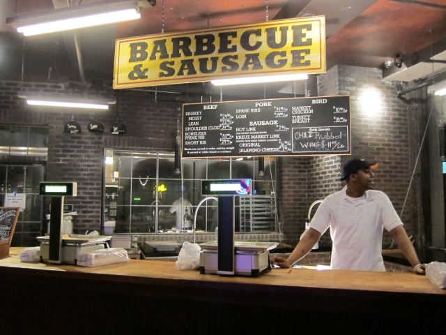 An employee of Hill Country Barbecue stands at the ordering counter in front of the menu