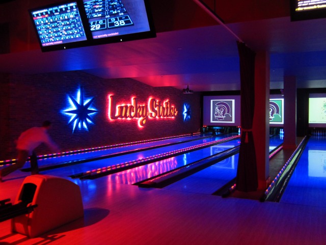 A man throwing a ball at Lucky Strike's bowling lanes lit up in red and blue.