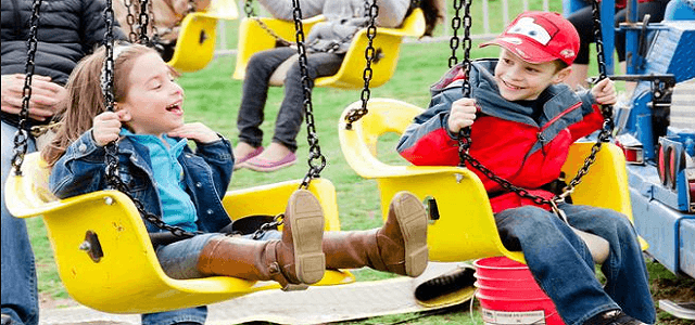 Two children swinging on a yellow swing set in a NYC park.