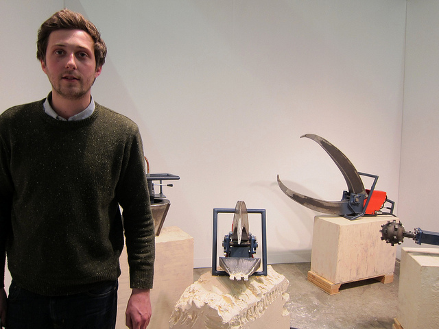 James Capper standing in front of an exhibition of mechanical tools sitting on while cement blocks at the Armory Show in NYC