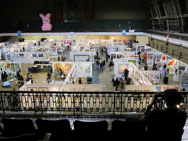 Ariel shot of people enjoyed the artwork at the armory art show in a large building with art hanging a maze of white pop-up walls