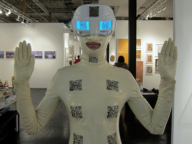 At the Scope Art Fair, a man is dressed up in a white body suit with QR codes on it and a glowing blue mask