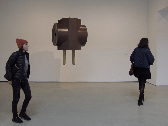 Two women walking around a piece by Claes Oldeburg, a big electrical plug that hangs from the ceiling