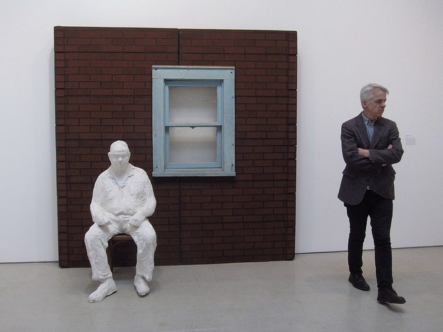 Man standing in Hauser and Wirth's Onnasch Collection with a portion of a brick wall and a white statue of a man sitting in a chair.