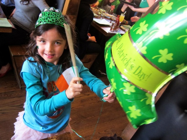 Young girl playing with green Irish hat balloon for St. Patrick's Day 