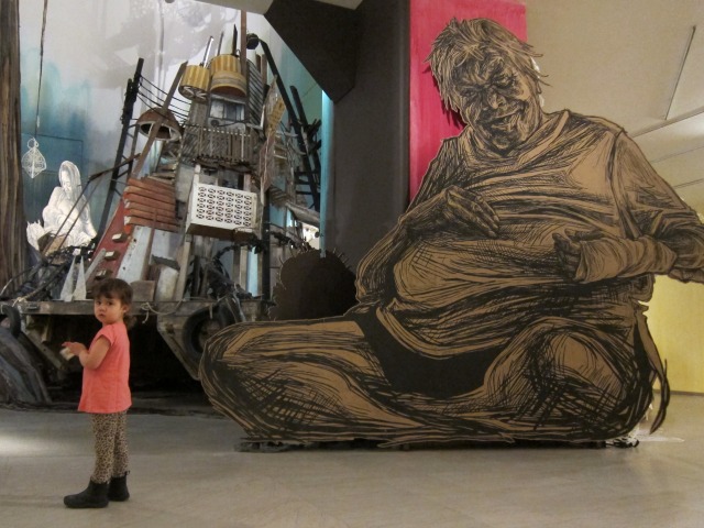 Image of a little girl standing infront of Swoon's intricately stenciled wheatpaste of a man sitting cross-legged