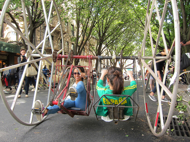 Image of two girls riding a crazy bike contraption with two opposite facing seats and large wheels in Central Park