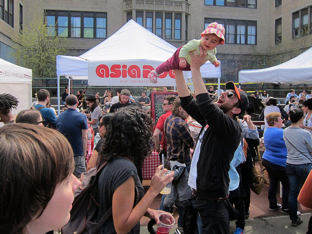 A man stands out of the crowds at the Brooklyn Flea market as he raises his baby up in the air playfully
