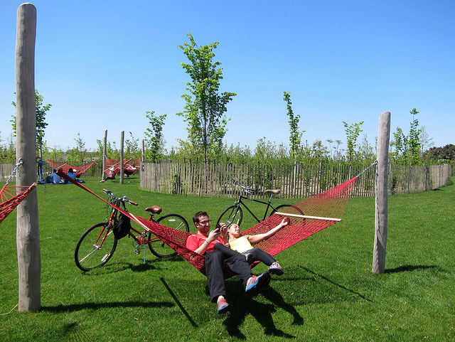 A couple relaxes on a bright red hammock in the open green lawn at Governors Island