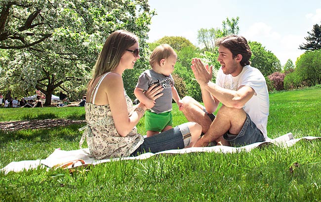 A couple with their baby sitting on a blanket having a picnic at the New York Botanical Garden