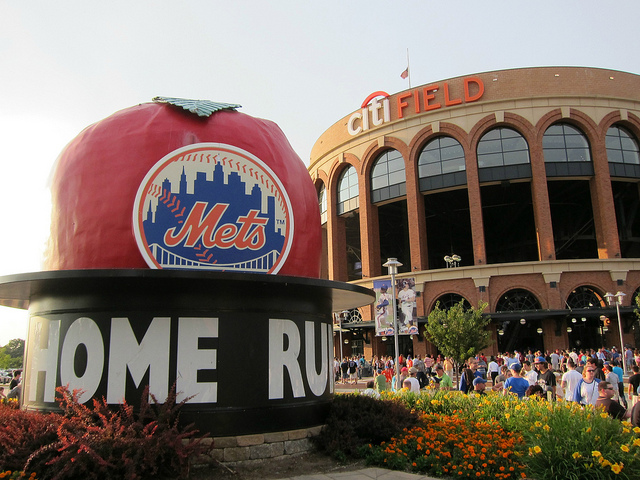 Crowds forms in front of Citi Field stadium and an apple statue with the Mets logo on in it and the text "Home Run"