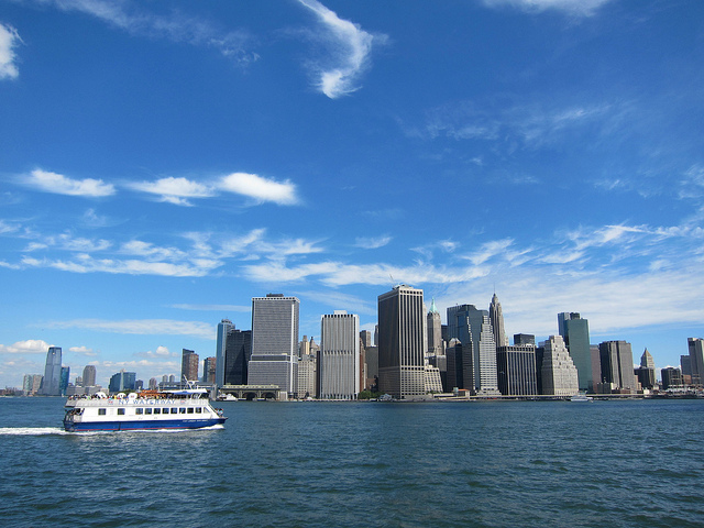 An image of a cruise boat on the river floating past the New York City skyline