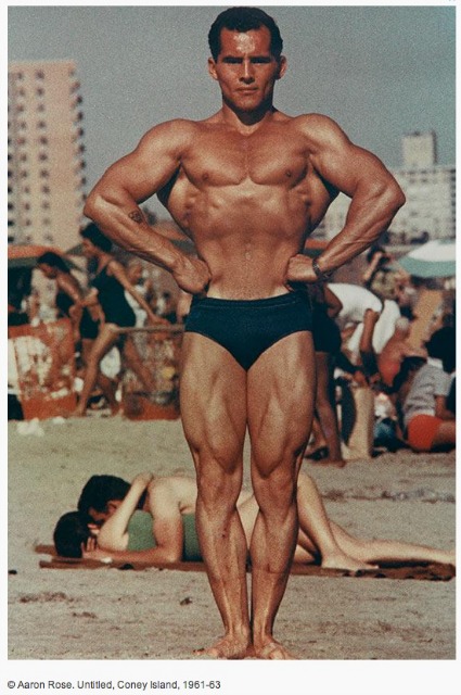 Vintage photograph of a muscular man in a black speedo with his hands on his hips standing on the beach at Coney Island