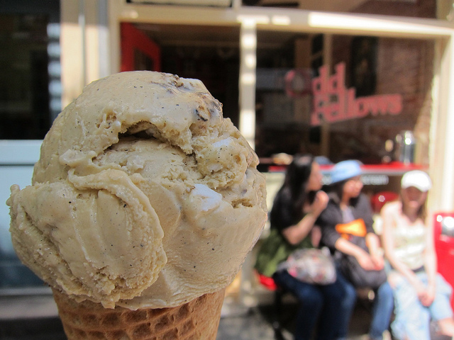 A scoop of ice cream melts in the foreground of NYC ice cream parlor, Odd Fellows, as three female patrons sit in the background, enjoying a frozen treat.