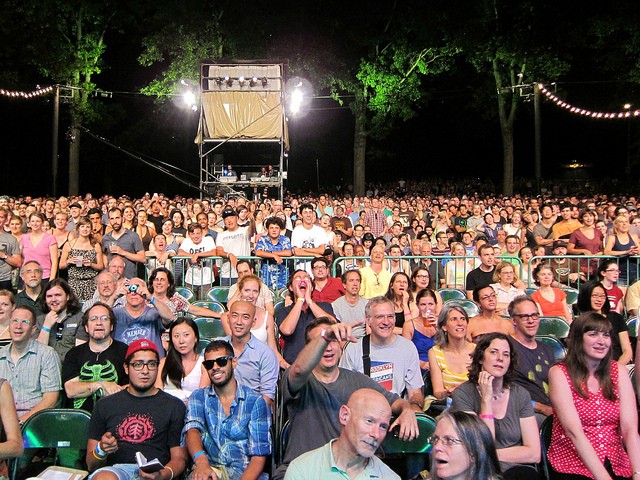 A crowded stadium seating area yells with excitement for Celebrate Brooklyn in Prospect Park