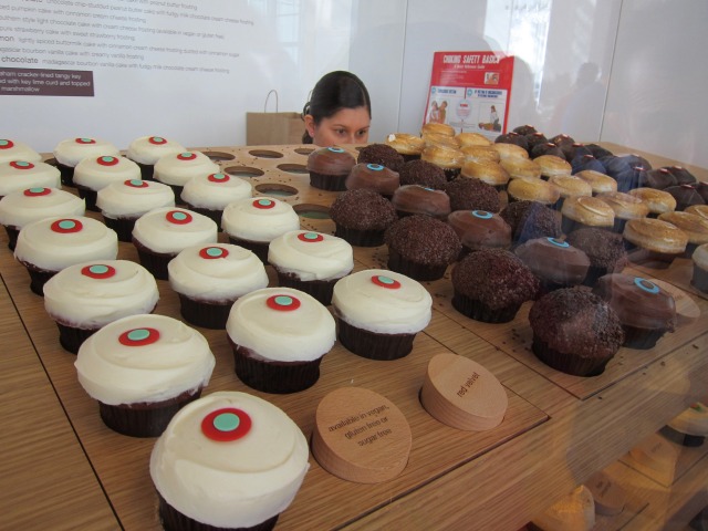 A women crouches down to admire Sprinkles' cupcake display with vanilla, chocolate and peanut butter selections.