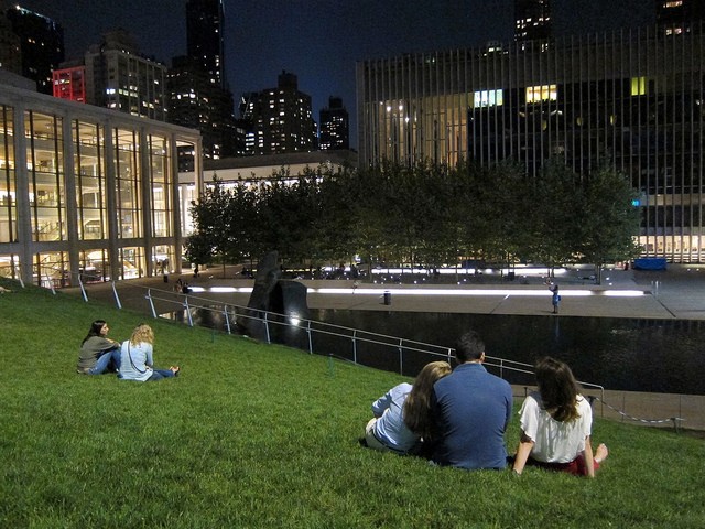 People sitting enjoying the view at Lincoln Center illumination lawn at night with the lights from the building glowing