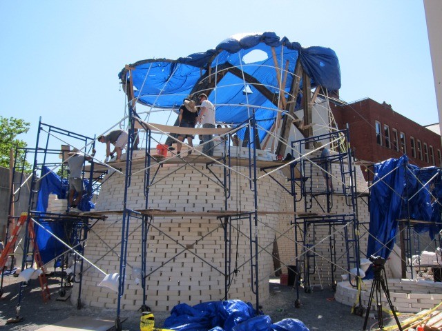 The MoMA PS1 Warm Up courtyard installation under construction with men climbing up on ladders