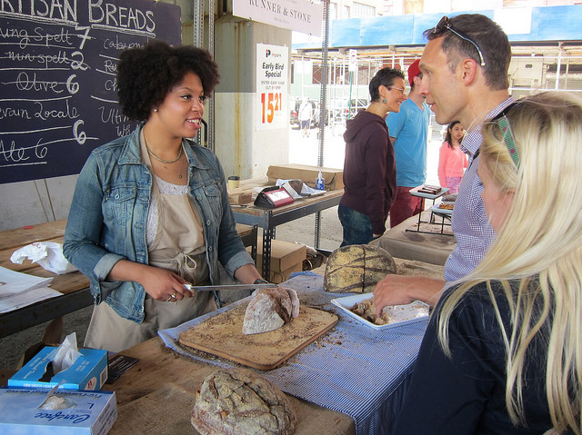 Women helps a customer try some of the Orwashers bread at a NYC outdoor food market.