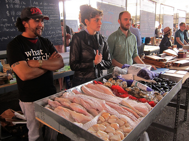 Three employees of the Village Fishmongers, man their stand at the New Amsterdam Market, selling fish and other seafood.