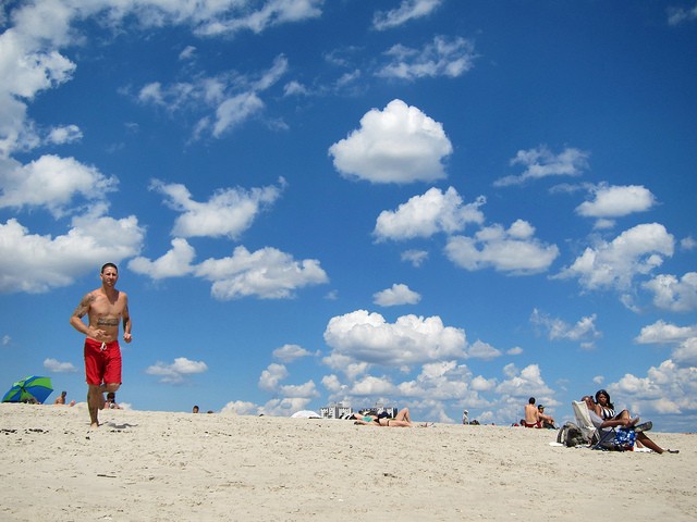 An image of beautiful blue skies and a man running through the sand at Rockaway Beach 67.