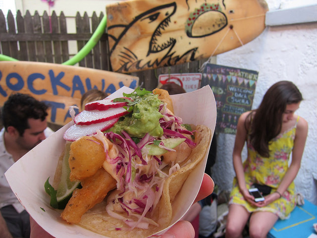 Close up image of one of the fish tacos at Rockaway Taco, topped with lettuce, guacamole and radishes.