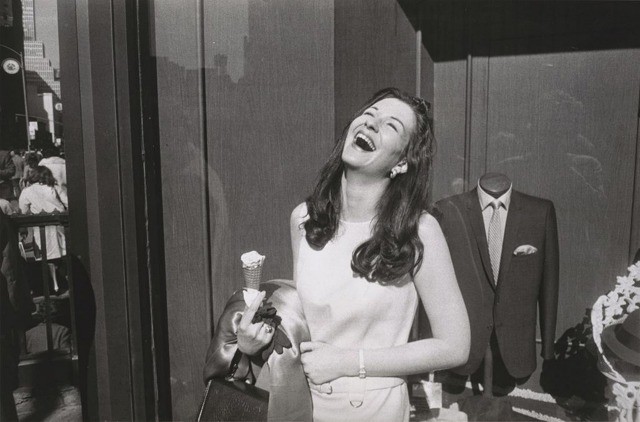 A photograph taken by Garry Winogrand of a women laughing, holding her purse and a half eaten ice cream cone.