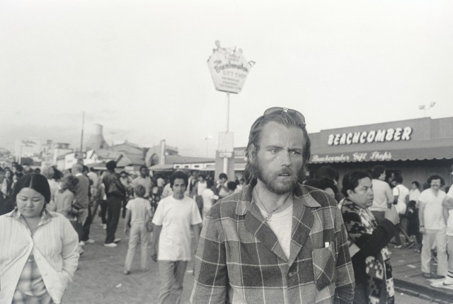 Image of a man with a twisted look on his face walking through the crowded streets of Santa Monica Pier.