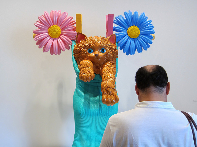 Balding man looking at a sculpture or a  cat in a sock on a clothesline.