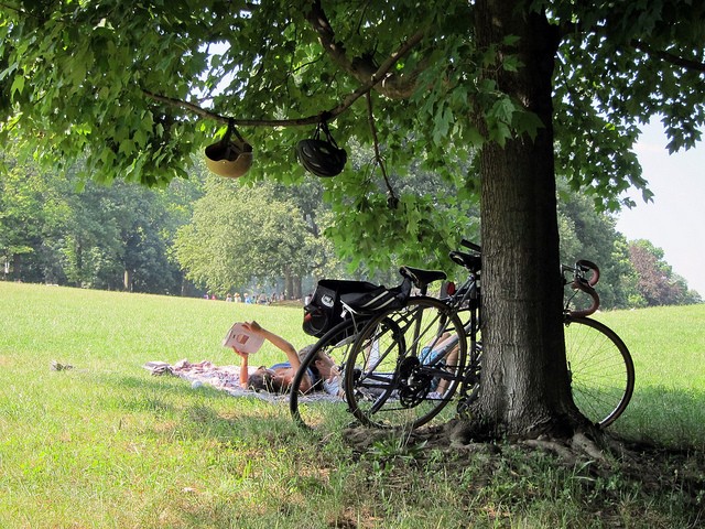 Two people ride their bike up to Prospect Park to lay out a blanket and read a book in the open green park