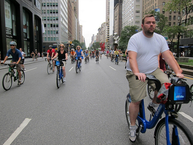 A large group of New York residents riding their bikes or citi bikes down the middle of the street in NYC.