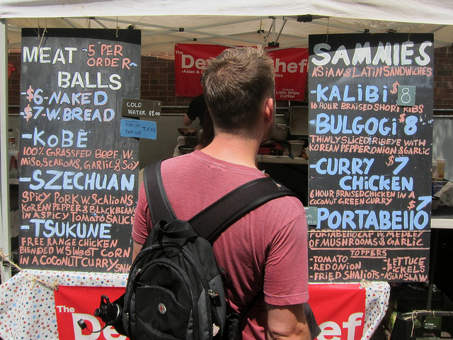 Young man in a red t-shirt takes a long look at the menu for Sammies at the Hester Street Fair